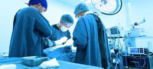 A SURGICAL TECHNOLOGIST LOOKS ON AS SURGEONS WORK ON A PATIENT