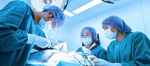 A SURGICAL TECH TRAINEE WATCHES AS A SURGEON PERFORMS A MEDICAL PROCEDURE