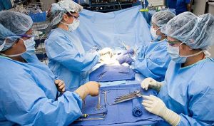 A SURGICAL TECHNOLOGIST HANDS THE SURGEON AN INSTRUMENT